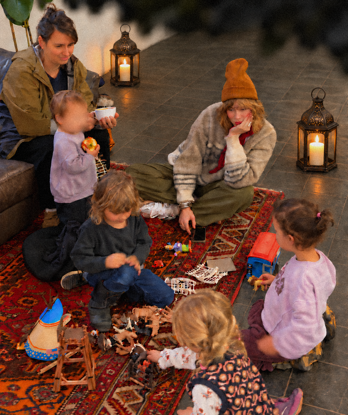 Kinder spielen auf dem Teppich, daneben Eltern mit Kaffee