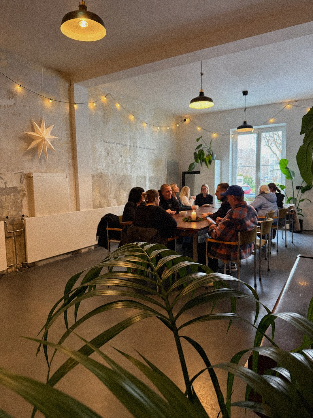 Gäste an der langen Tafel im WerDerRaum, Stern und Lichterkette an der alten Wand